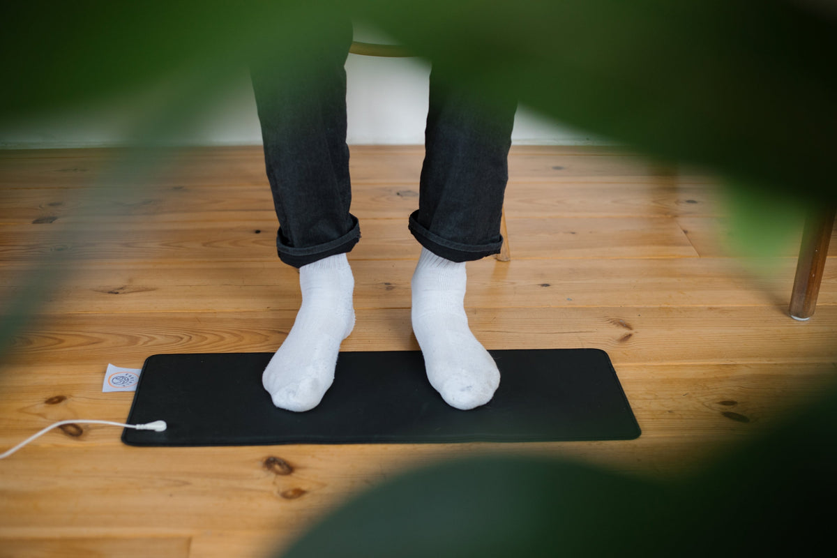 Voeten in witte sokken op een zwarte Earthle aardingsmat op een houten vloer