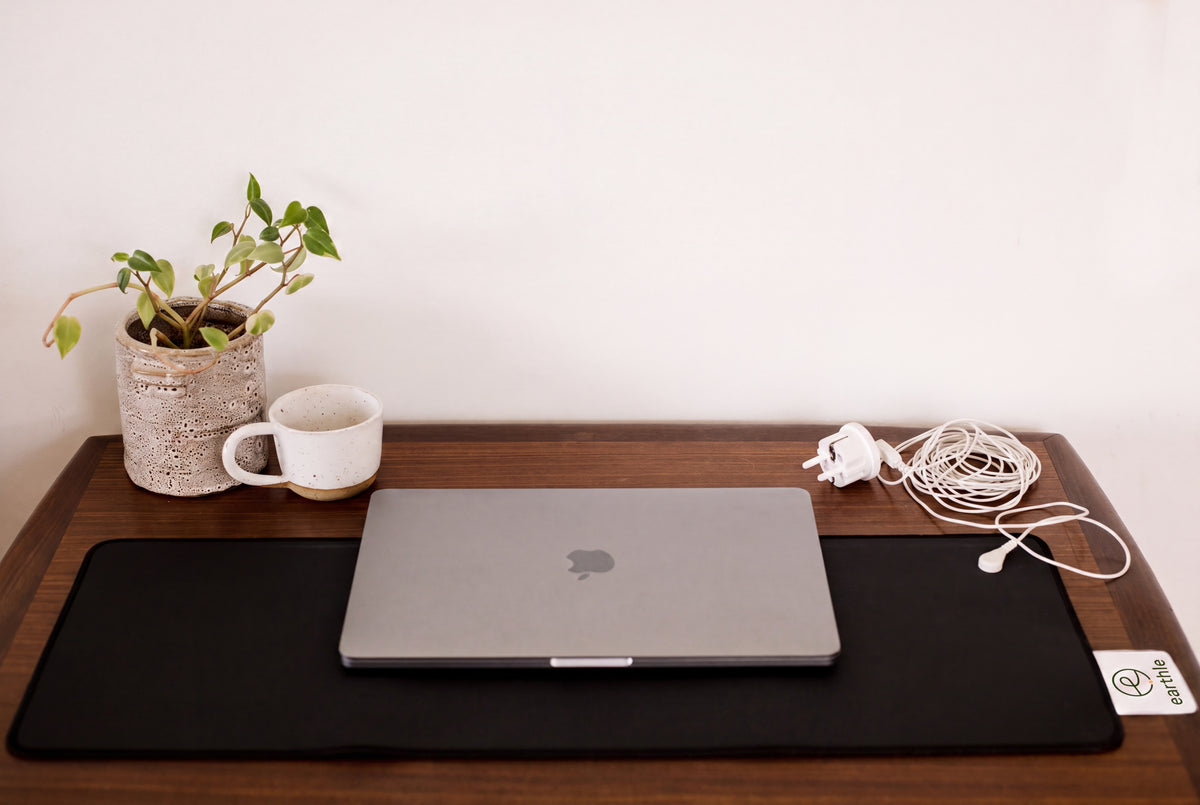 Werkplek met de Earthle aardingsbureaumat, een laptop, een plant, een beker en de opgerolde aardingskabel