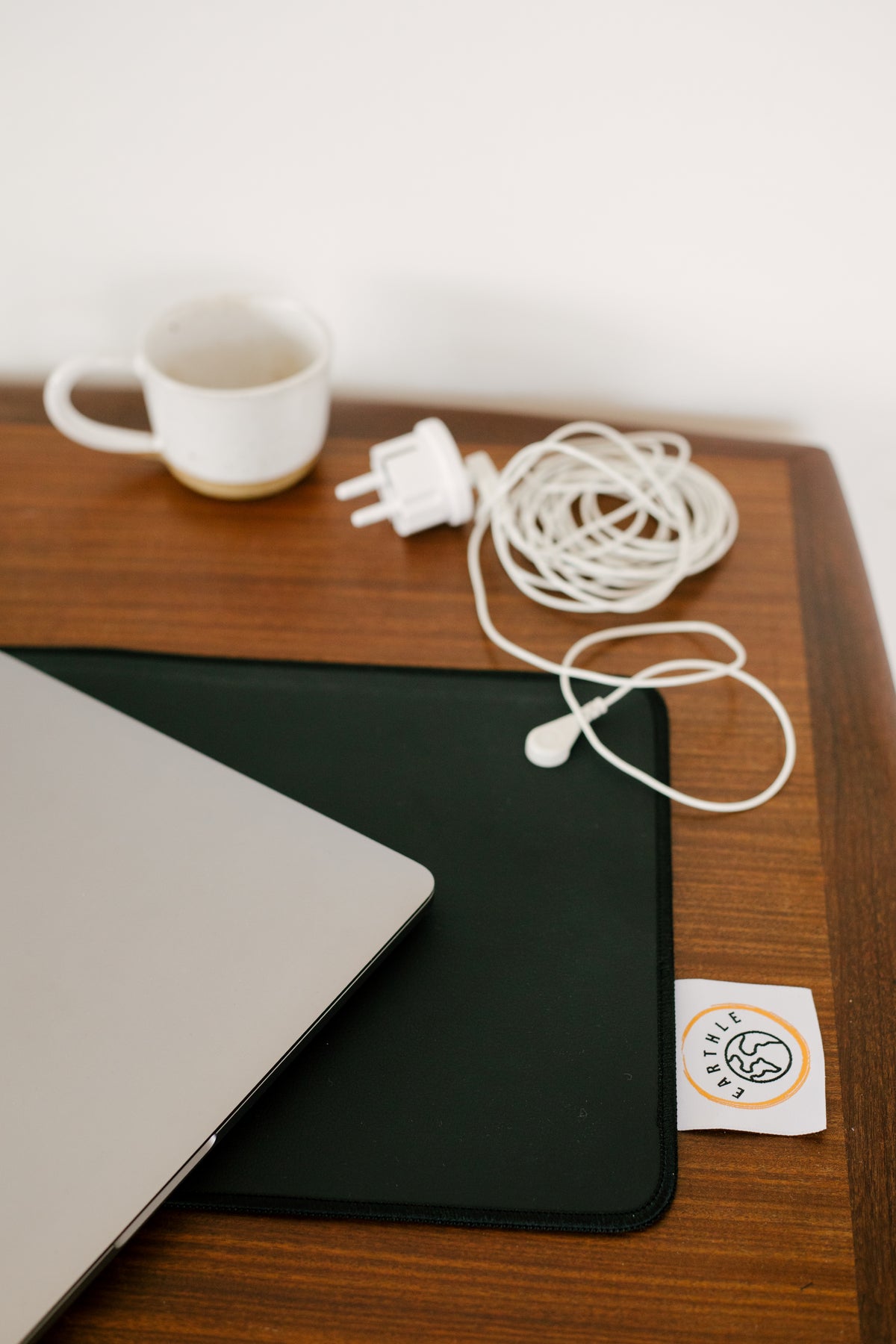 Jordningskontakt och upprullad kabel på ett skrivbord bredvid skrivbordsmattan och en bärbar dator